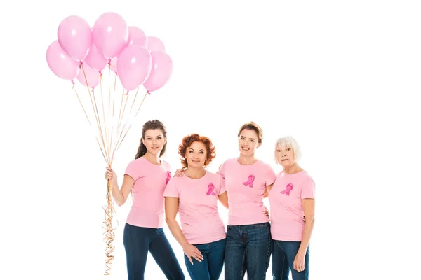 Mujeres con cintas de conciencia de cáncer de mama sosteniendo globos rosados y sonriendo a la cámara aislada en blanco - foto de stock