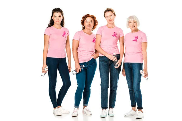 Mulheres em camisetas rosa com fitas de consciência de câncer de mama segurando garrafas de água e olhando para a câmera isolada em branco — Fotografia de Stock