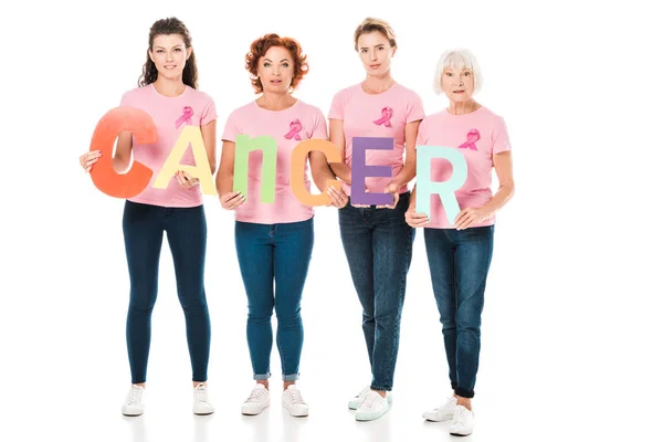 Women in pink t-shirts with breast cancer awareness ribbons holding colorful letters with word cancer and looking at camera isolated on white — Stock Photo
