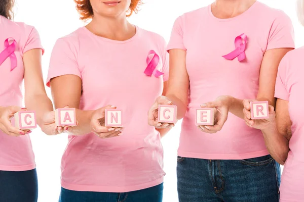 Inyección recortada de mujeres en camisetas de color rosa con cintas de conciencia de cáncer de mama que sostienen cubos con cáncer de palabra aislado en blanco - foto de stock