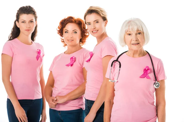Mujeres en camisetas de color rosa con cintas de conciencia de cáncer de mama y médico senior con estetoscopio sonriendo a la cámara aislada en blanco - foto de stock