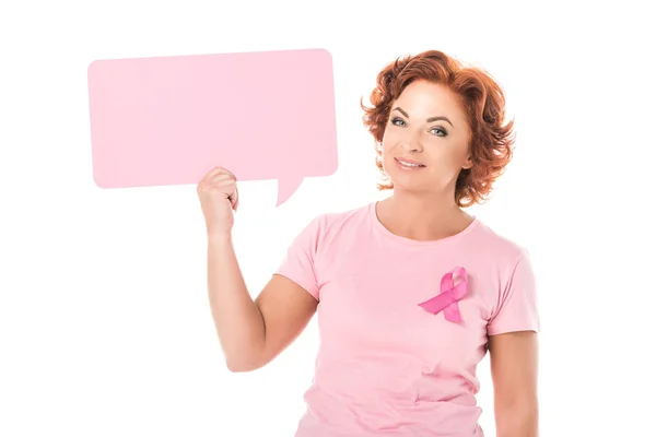 Женщина среднего возраста в розовой футболке с лентой информированности о раке молочной железы держит пустой пузырь речи и улыбается в камеру, изолированную на белом — стоковое фото