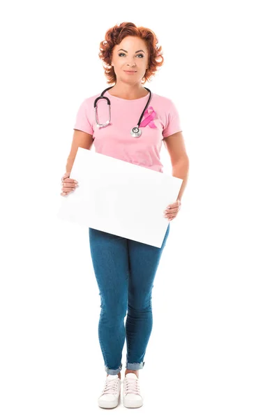 Mujer madura con estetoscopio sosteniendo pancarta en blanco y mirando a la cámara aislada en blanco, concepto de conciencia de cáncer de mama - foto de stock