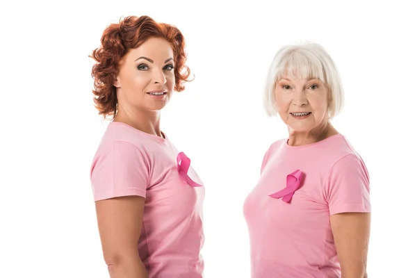 Vue latérale des femmes avec des rubans roses souriant à la caméra isolée sur blanc, concept de sensibilisation au cancer du sein — Photo de stock