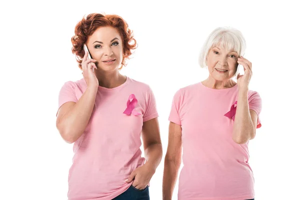 Mujeres con cintas de color rosa hablando con teléfonos inteligentes y sonriendo a la cámara aislada en blanco, concepto de conciencia de cáncer de mama - foto de stock