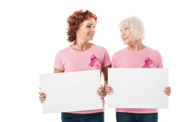 Women with pink ribbons holding blank banners and smiling each other isolated on white, breast cancer awareness concept — Stock Photo