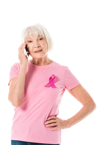 Senior woman in pink t-shirt with breast cancer awareness ribbon talking by smartphone and looking at camera isolated on white — Stock Photo