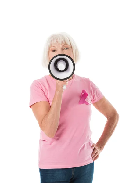 Femme âgée en t-shirt rose avec ruban de sensibilisation au cancer du sein tenant le mégaphone et regardant la caméra isolée sur blanc — Photo de stock