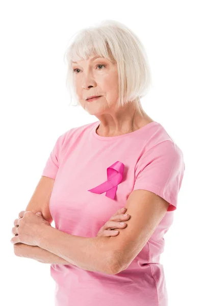 Mujer mayor en camiseta rosa con cinta de sensibilización sobre el cáncer de mama de pie con los brazos cruzados y mirando hacia otro lado aislado en blanco - foto de stock