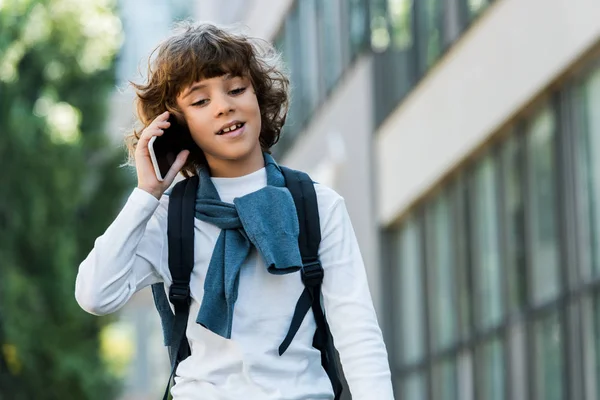 Low angle view of schoolboy with backpack talking by smartphone and looking down — Stock Photo
