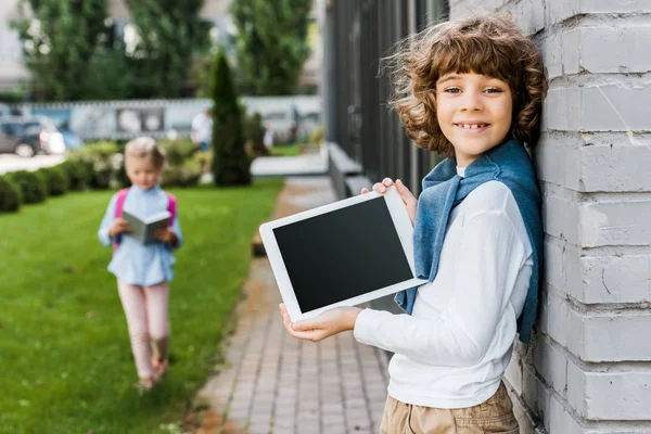 Mignon garçon heureux tenant tablette numérique avec écran blanc et souriant à la caméra — Photo de stock