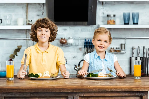 Entzückende Kinder essen Gemüse und lächeln in die Kamera in der Küche — Stockfoto