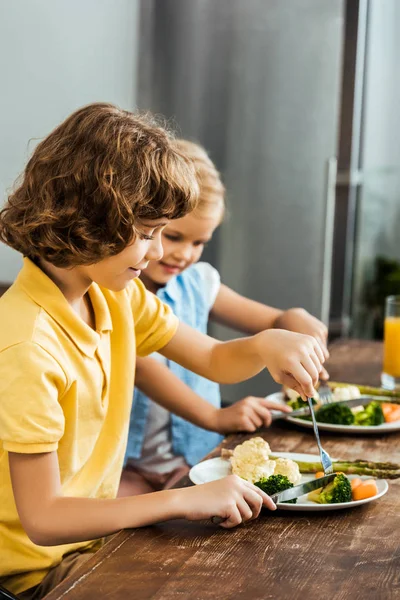 Vista lateral de crianças felizes bonitos comer legumes saudáveis — Fotografia de Stock