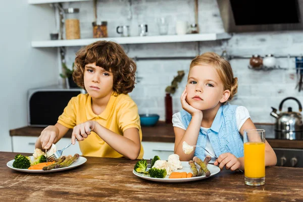 Ennuyé enfants manger des légumes et regarder la caméra — Photo de stock
