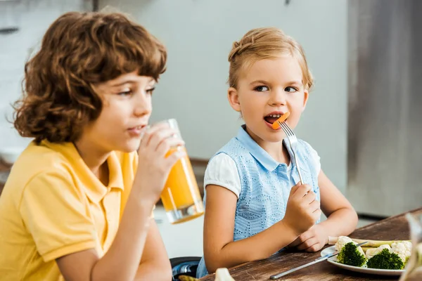 Niños pequeños y lindos comiendo verduras y bebiendo jugo - foto de stock