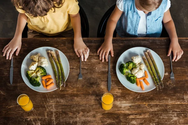 Cropped shot of cute little kids eating healthy vegetables at wooden table — Stock Photo