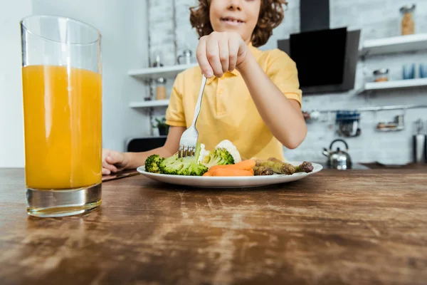 Крупный план свежего сока в стакане и улыбающегося мальчика, поедающего овощи — стоковое фото