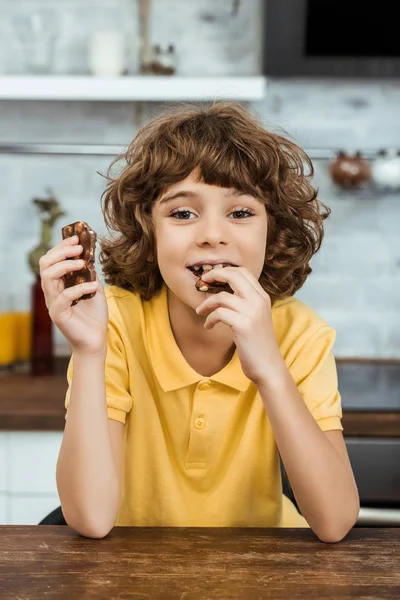 Süßer glücklicher Junge isst leckere Schokolade mit Nüssen und lächelt in die Kamera — Stockfoto