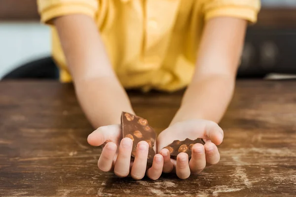 Nahaufnahme: Kind hält leckere Schokoladenstücke mit Haselnüssen in der Hand — Stockfoto