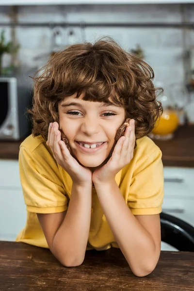 Lindo niño feliz sosteniendo trozos de delicioso chocolate y sonriendo a la cámara - foto de stock