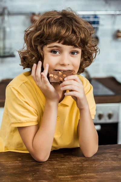 Lindo niño comiendo chocolate con avellanas y mirando a la cámara - foto de stock