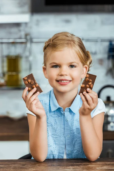 Adorable niño feliz sosteniendo trozos de delicioso chocolate y sonriendo a la cámara - foto de stock