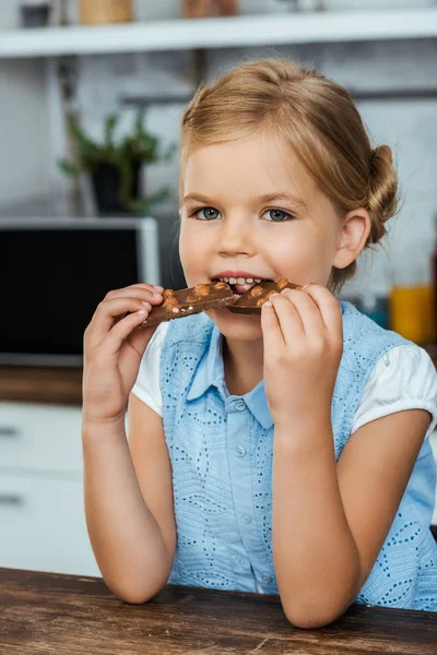 Entzückendes Kind isst leckere Schokolade mit Haselnüssen und lächelt in die Kamera — Stockfoto