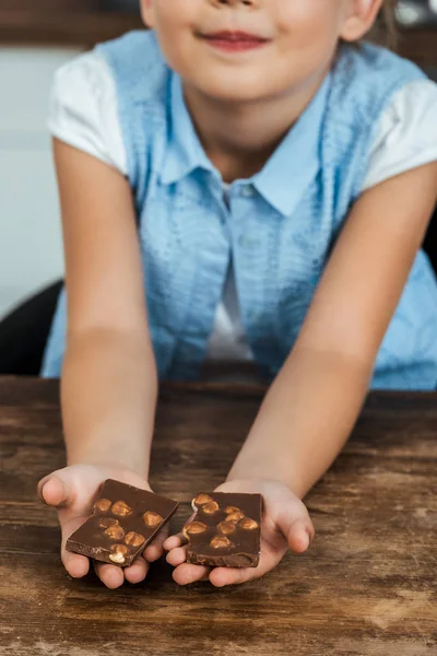 Gros plan vue partielle d'un enfant souriant tenant des morceaux de chocolat sucré aux noisettes — Photo de stock