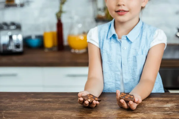 Cropped shot of smiling child holding pieces of sweet chocolate with hazelnuts — Stock Photo
