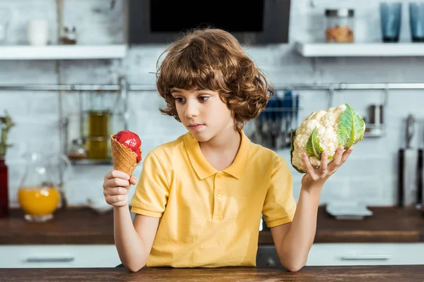 Niño sosteniendo delicioso helado dulce y coliflor saludable - foto de stock