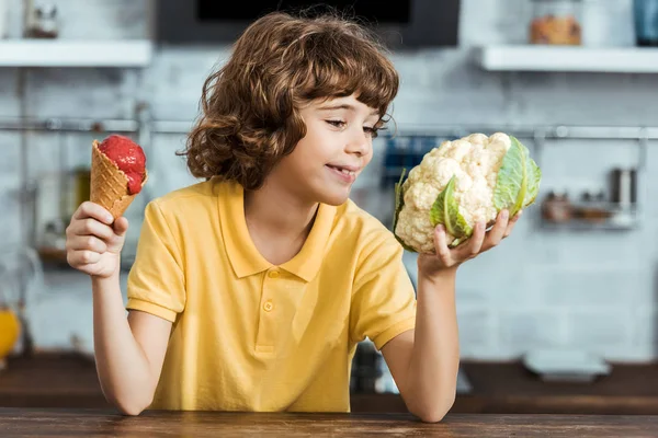 Lindo niño sonriente sosteniendo helado dulce y coliflor saludable - foto de stock