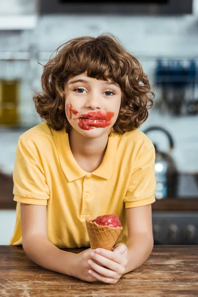 Adorable boy with ice cream on face holding delicious ice cream cone and looking at camera — Stock Photo
