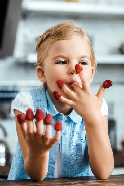 Lindo niño feliz sentado en la mesa y comer frambuesas frescas maduras - foto de stock