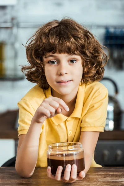 Cute happy boy eating chocolate spread from container and looking at camera — Stock Photo