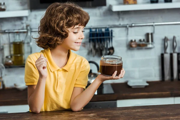 Cute happy little boy holding glass jar with delicious chocolate spread — Stock Photo