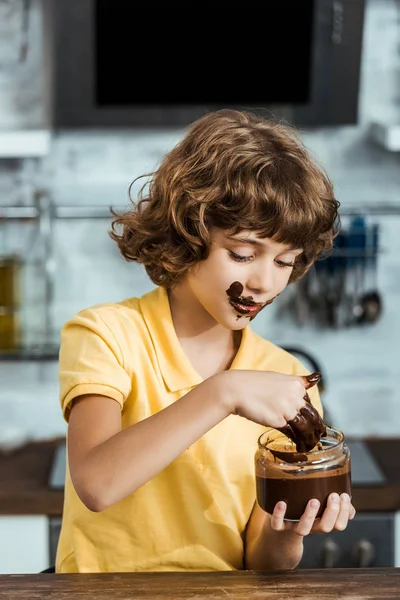 Cute little boy eating sweet chocolate spread from glass jar — Stock Photo