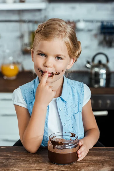 Adorable niño comiendo delicioso chocolate propagación y sonriendo a la cámara - foto de stock