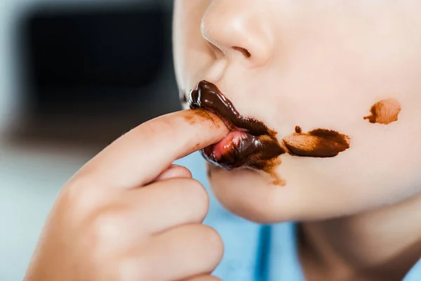 Recortado tiro de niño lamiendo dedo con delicioso chocolate propagación - foto de stock