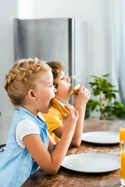 Vue latérale de mignons petits enfants mangeant de savoureux sandwichs — Photo de stock