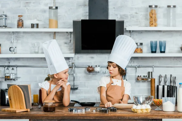 Adorables petits enfants dans des chapeaux de chef et tabliers de cuisine ensemble dans la cuisine — Photo de stock