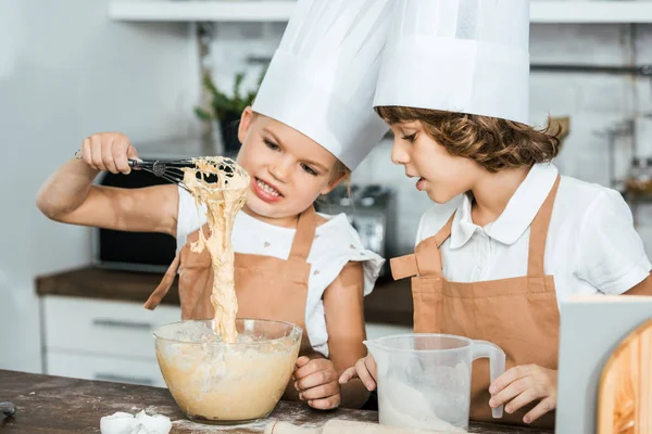 Petits enfants mignons dans des tabliers et des chapeaux de chef préparant la pâte pour les biscuits savoureux ensemble — Photo de stock