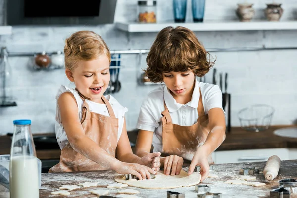 Crianças sorridentes adoráveis em aventais que preparam a massa de farinha de biscoitos saborosos — Fotografia de Stock