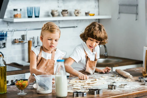 Crianças adoráveis em aventais que preparam a massa de farinha de biscoitos saborosos — Fotografia de Stock