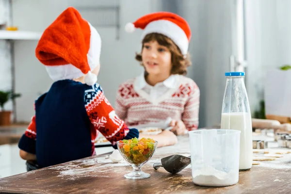 Adorable kids in santa hats looking at each other while cooking together — Stock Photo