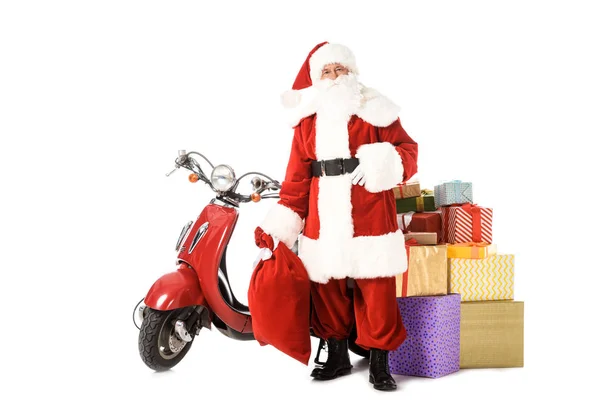 Weihnachtsmann steht mit rotem Oldtimer-Roller, Sack und Geschenkschachteln und schaut vereinzelt in die Kamera auf weißem Grund — Stockfoto