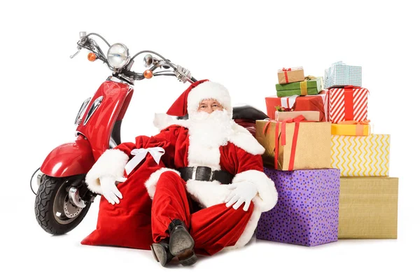 Tired santa claus sitting on floor with vintage red scooter, sack and gift boxes isolated on white — Stock Photo