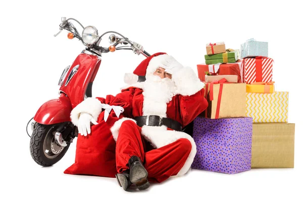 Exhausted santa claus sitting on floor with vintage red scooter, sack and gift boxes isolated on white — Stock Photo