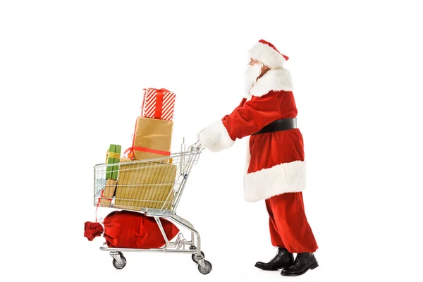 Vista lateral de santa claus andando com carrinho de compras cheio de caixas de presente de Natal isolado no branco — Fotografia de Stock