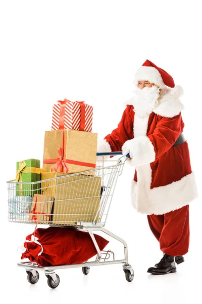 Weihnachtsmann zu Fuß mit Einkaufswagen voller Geschenkboxen isoliert auf weiß — Stockfoto