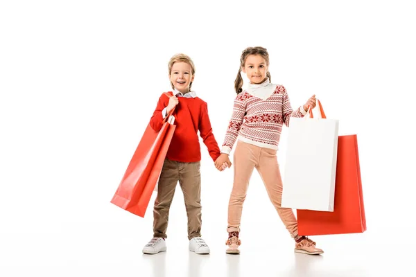 Прелестные маленькие дети в рождественском свитере с большими бумажными пакетами, изолированными на белом — стоковое фото